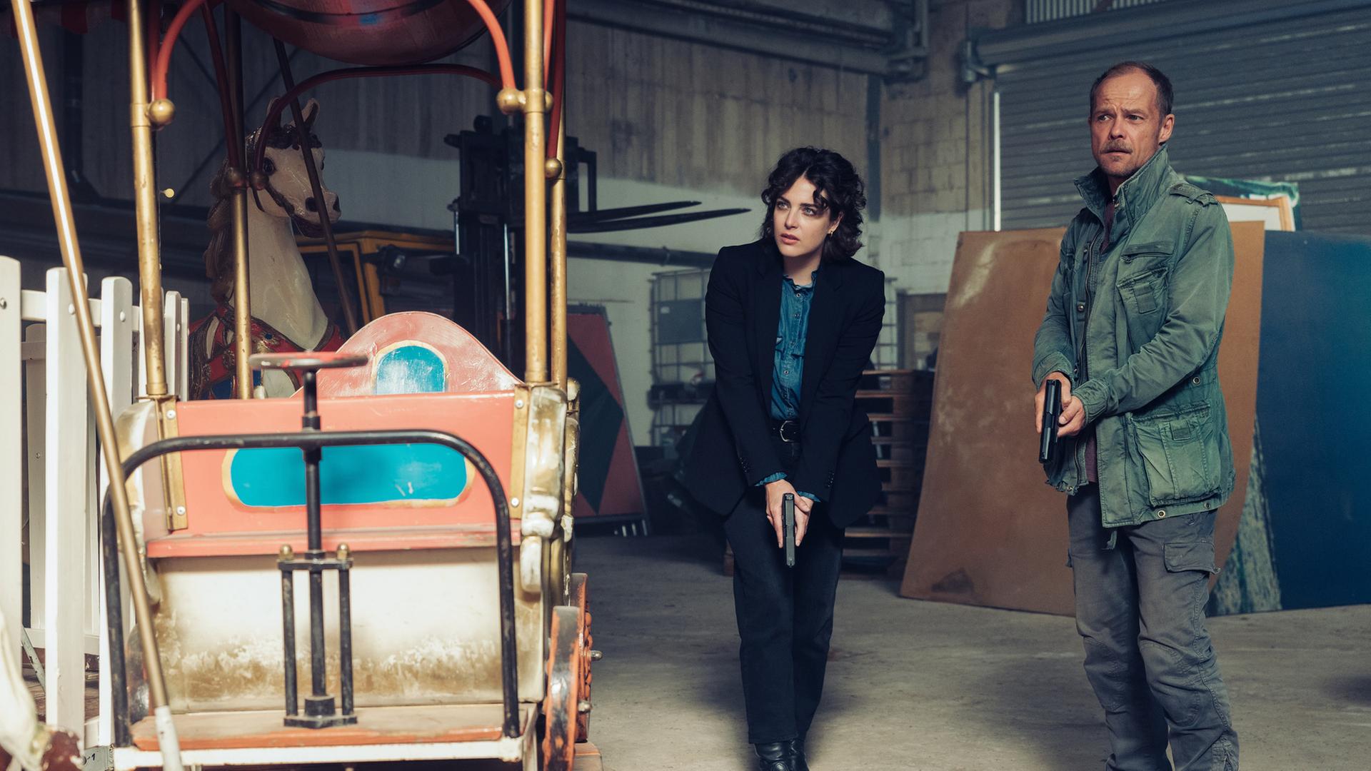  "Die Toten vom Bodensee - Schicksalsrad": Mara Eisler (Anna Werner Friedmann) und Micha Oberländer (Matthias Koeberlin) stehen mit gezogener Waffe in einer Lagerhalle.