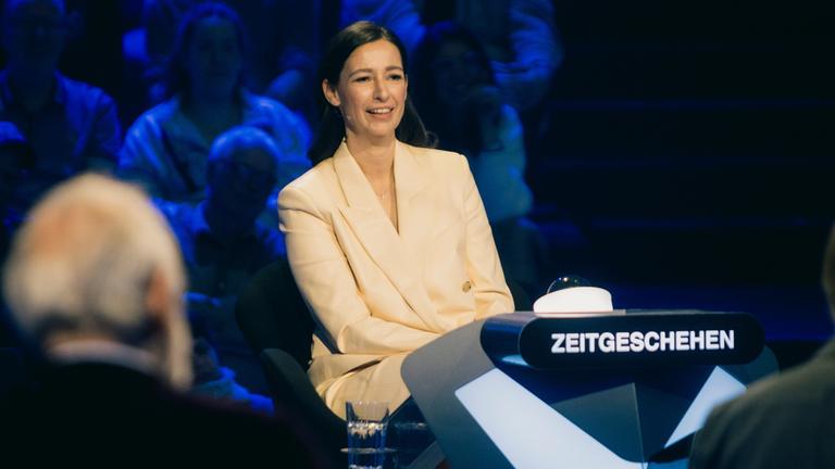 "Der Quiz-Champion": Pinar Atalay sitzt im Studio an einem Pult, hinter ihr befindet sich das Publikum.