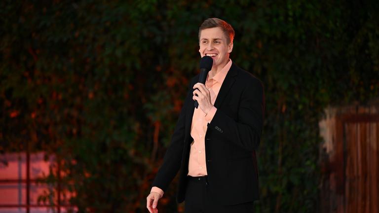  "ZDF Comedy Sommer mit Till Reiners": Till Reiners steht mit einem Mikrofon in der Hand auf der Bühne und lächelt Richtung Publikum.