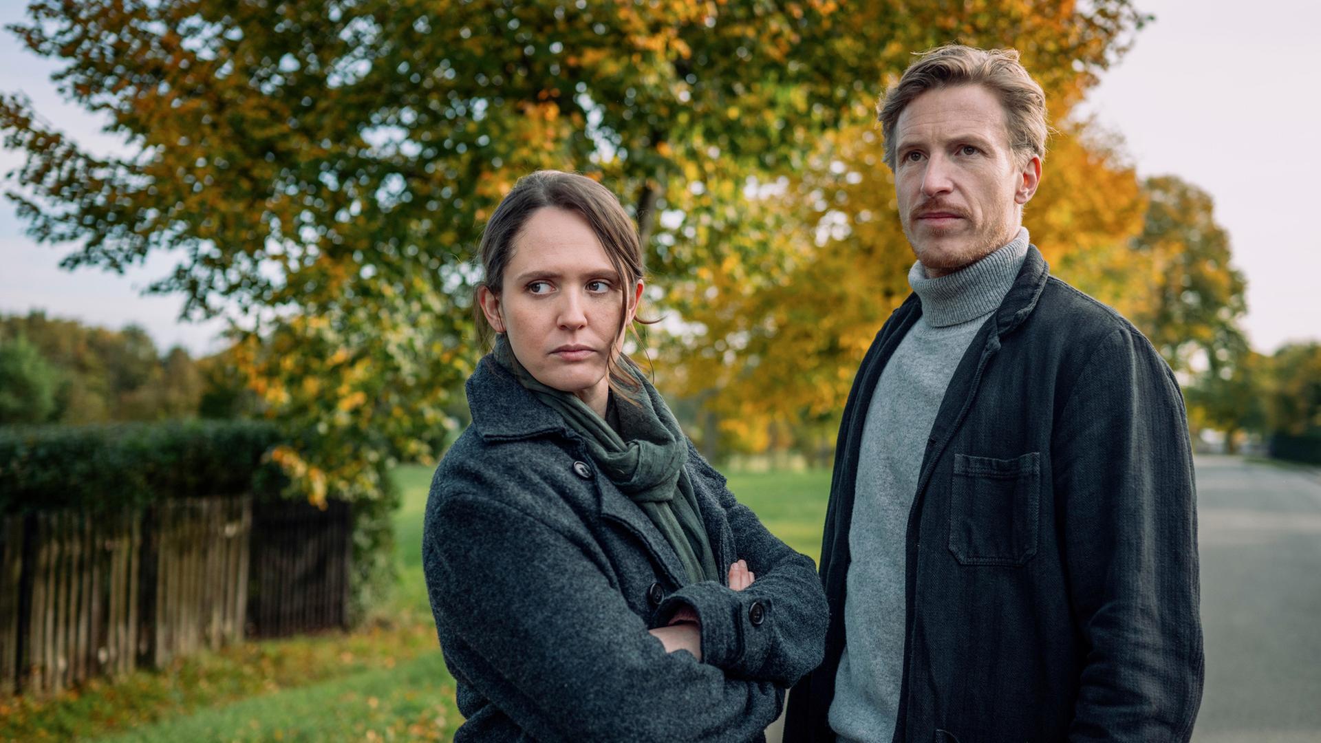 "Thüringenkrimi - Gerechtigkeit": Auf einer ländlichen Straßen steht Mala Murphy (Emily Cox) mit verschränkten Armen und schaut zur Seite. Daneben steht Moritz Herbst (Golo Euler) und schaut in die selbe Richtung.