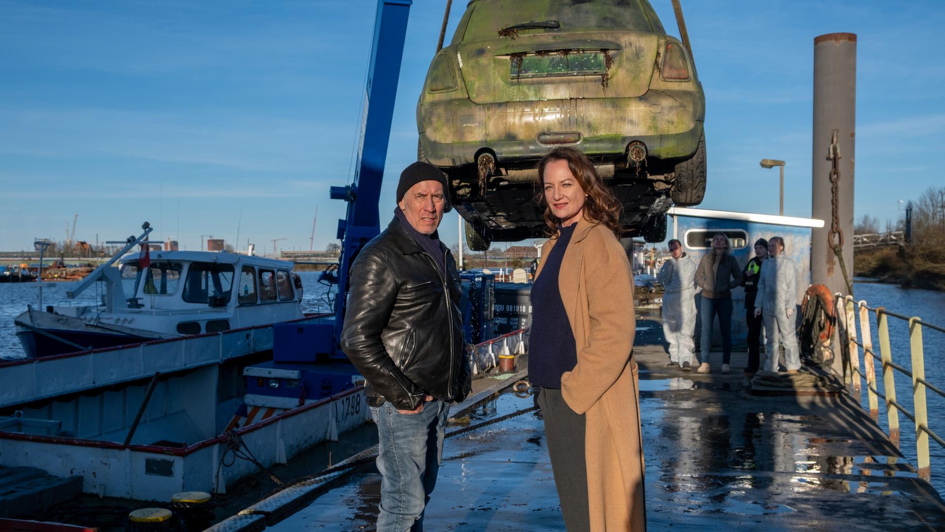 "Unter anderen Umständen - Das Mädchen ohne Namen": Matthias Hamm (Ralph Herforth) und Jana Winter (Natalia Wörner) stehen an Hafen. Hinter ihnen holt ein Kran ein Auto aus dem Wasser, daneben stehen einige Kollegen der Spurensicherung (Komparsen).