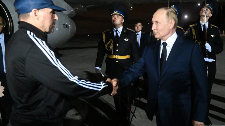 "Putins Schattenkrieger - Russische Agenten packen aus": Präsident Putin begrüßt den Tiergartenmörder von Berlin, Wadim Krassikow. Beide stehen nachts vor einem Flugzeug. Im Hintergrund stehen mehrere Personen in Uniform.