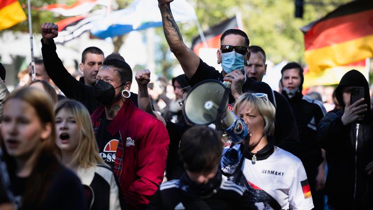 Rechtsradikaler Protestdemonstration. Die Teilnehmer schwenken zum Teil Deutschlandfahnen und recken die Fäuste nach oben. Eine Frau in einem T-Shirt mit dem Aufdruck "Germany" spricht in ein Megaphon.  