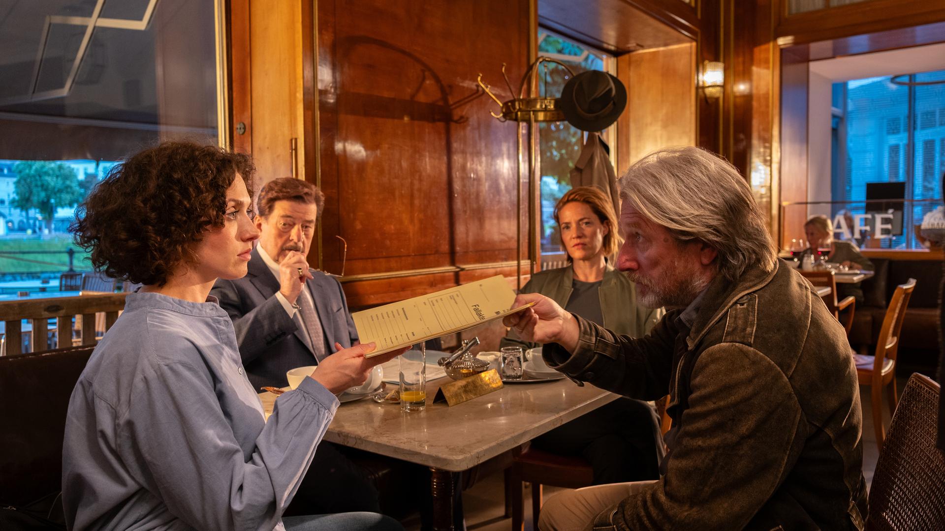  "Die Toten von Salzburg - Die letzte Reise": Irene Russmeyer (Fanny Krausz), Alfons Seywald (Erwin Steinhauer), Lu Frey (Patricia Aulitzk.) und Hubert Mur (Michael Fitz) sitzen zusammen im Café. Hubert Mur übergibt Irene Russmeyer eine Akte.