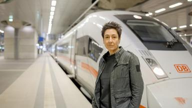 "Am Puls mit Dunja Hayali - Unsere Bahn: geliebt, verflucht - gefährlich?": Dunja Hayali steht in einer Bahnhofshalle auf einem leeren Gleis vor einem ICE und schaut in die Kamera.