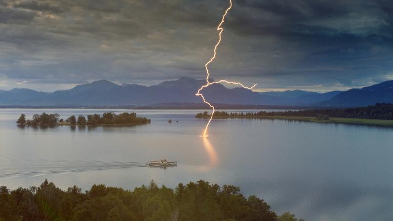 "Terra X: Blitze - Himmel unter Strom": Ein Blitz schlägt in die Wasseroberfläche des Chiemsees ein, während in der Nähe ein Schiff entlangfährt.