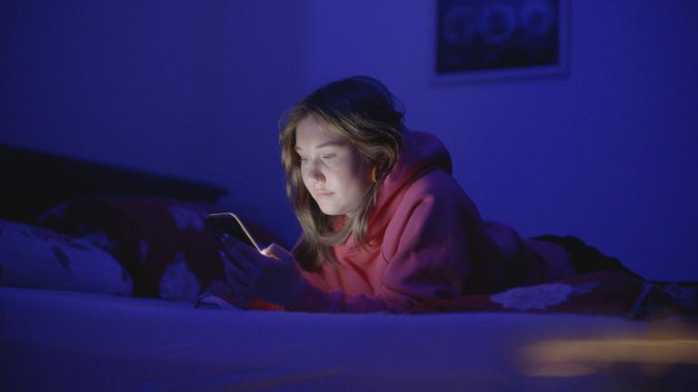 "Generation Porno - Was unsere Kinder online sehen": Paulina liegt auf ihrem Bett in einem dunklen Kinderzimmer und schaut auf ihr Smartphone.