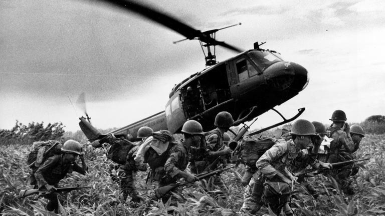 "Die Kriege der USA - Im Namen der Freiheit": Schwarz-Weiß-Foto: Ein Bell UH-1 "Huey“ Hubschrauber bringt im Vietnamkrieg Truppen ins Kampfgebiet: Er fliegt tief über einem Reisfeld in dem sich acht Soldaten befinden.