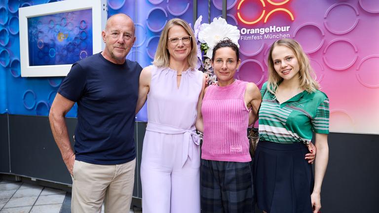 Filmfest München, Orange Hour: Von links: Heino Ferch, Nadine Bilke, Juli Zeh und Lili Epply stehen nebeneinander und lächeln in die Kamera.
