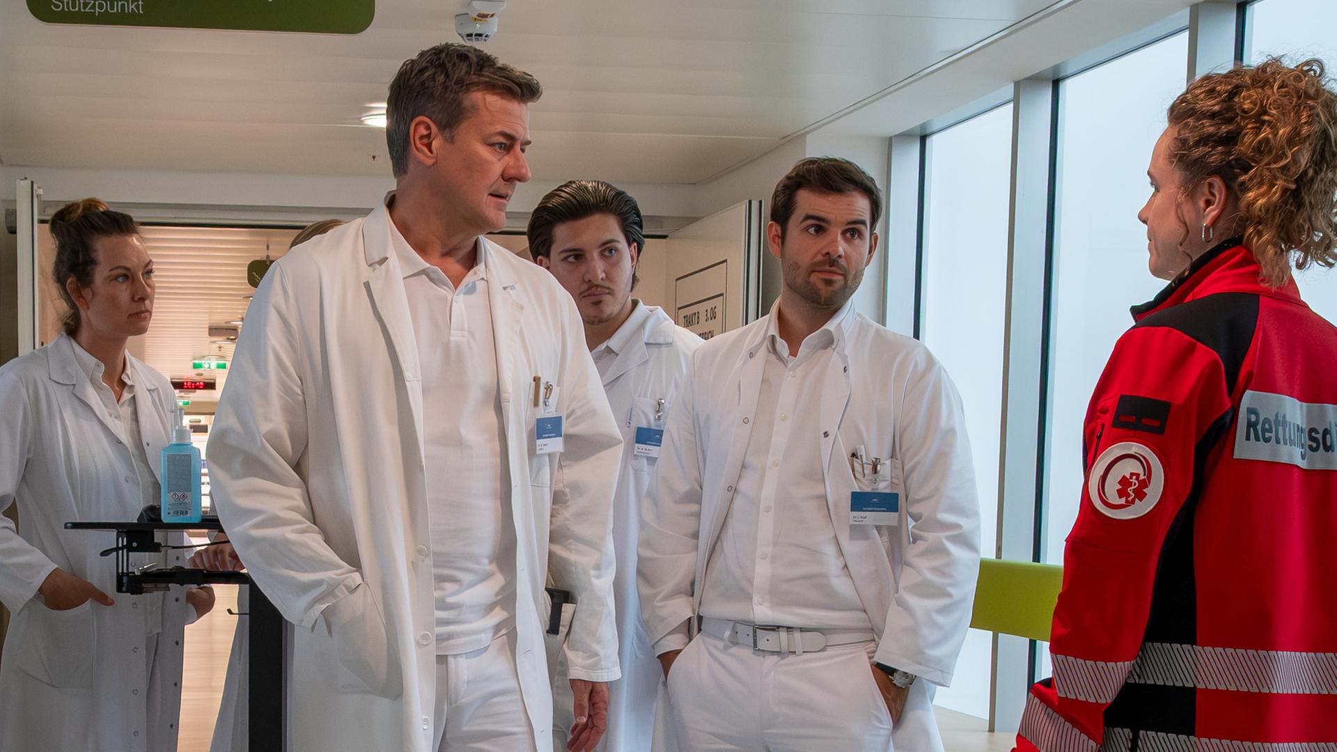 "Einfach Elli - Neuanfang": Elli Kempfer (Klara Deutschmann) steht mit Dr. Mark Sorell (Marcus Mittermeier) und Dr. Jasper Graf (Lucas Reiber) sowie weiteren Ärzten (Komparsen) im Krankenhausflur.