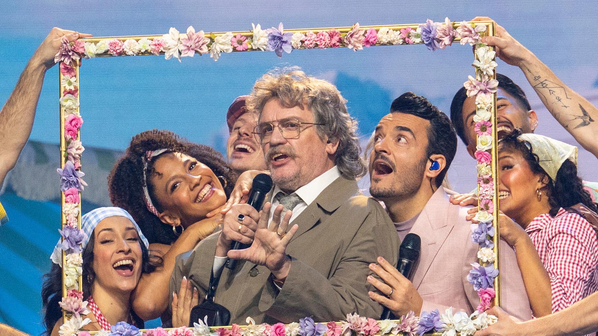  "Die Giovanni Zarrella Show - Ein Abend für die Liebe": Horst Schlämmer und Giovanni Zarrella stehen hinter einem mit Blumen dekorierten Bilderrahmen. Horst Schlämmer singt in ein Mikrofon. Um sie herum befinden sich Tänzerinnen und Tänzer.