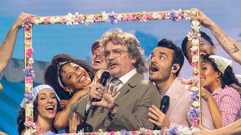  "Die Giovanni Zarrella Show - Ein Abend für die Liebe": Horst Schlämmer und Giovanni Zarrella stehen hinter einem mit Blumen dekorierten Bilderrahmen. Horst Schlämmer singt in ein Mikrofon. Um sie herum befinden sich Tänzerinnen und Tänzer.