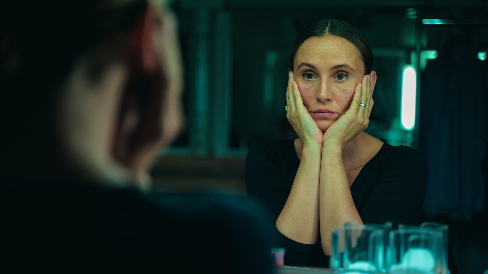 "Eine bessere Welt": Elena (Peri Baumeister) hat ihren Kopf in die Arme gestützt und blickt sich im Spiegel an.