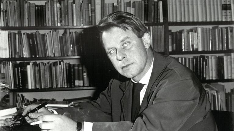 "Siegfried Lenz und die Kraft des Gewissens": Der junge Siegfried Lenz sitzt vor einer Bücherwand am Schreibtisch (s/w).