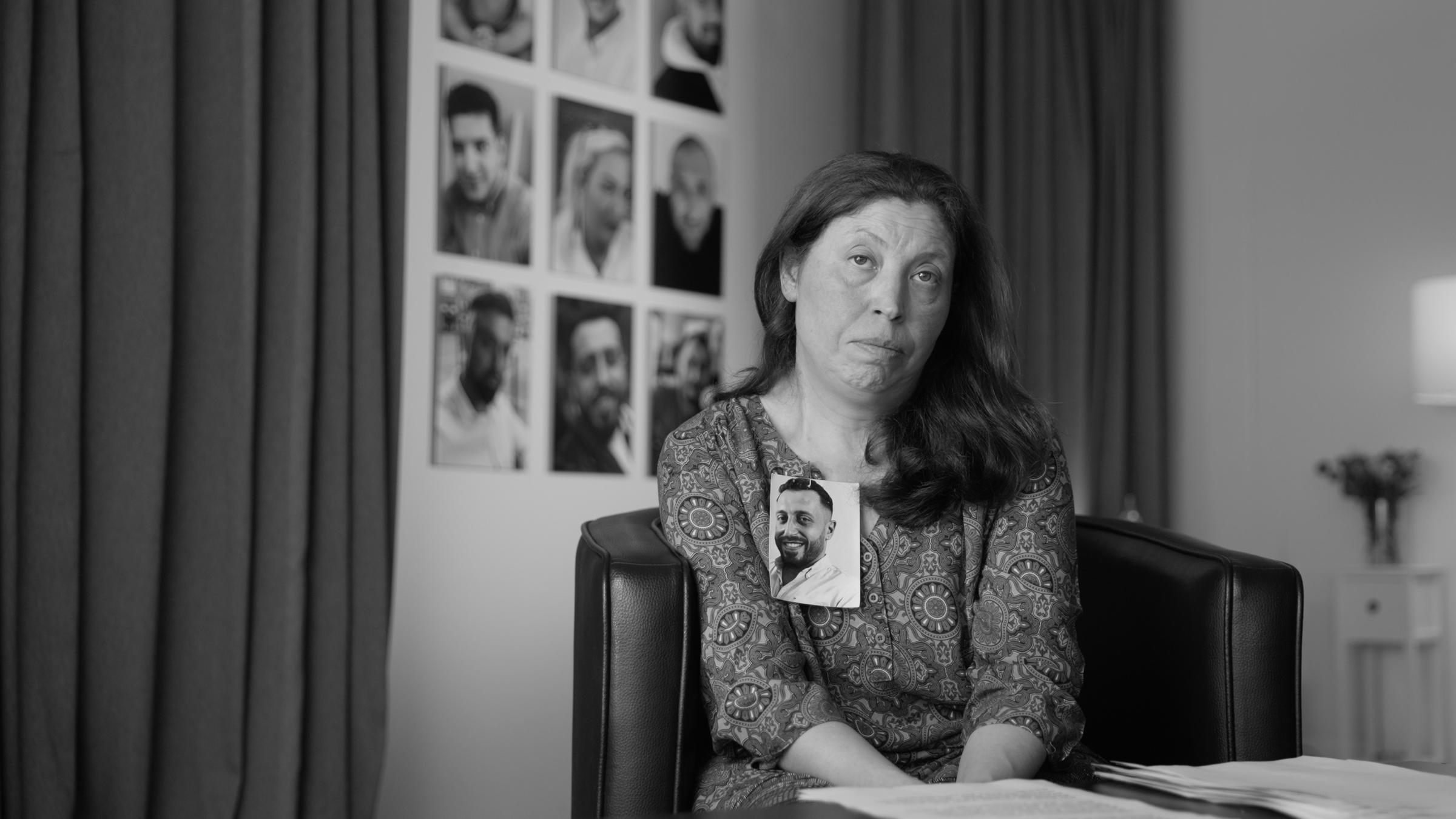 "Das Deutsche Volk": Frau blickt direkt in die Kamera. An ihrem Revers ist das Foto eines jungen Mannes befestigt.