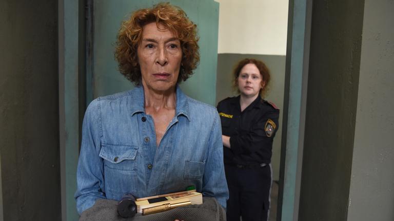 "Mama ist die Best(i)e Teil I": Gloria Almeda (Adele Neuhauser) trägt Gefängniskleidung. Sie wird von einer Justizbeamtin zu ihrer Zelle gebracht und hält einige Utensilien in Händen. Die Tür hinter ihr wird sich gleich schließen.