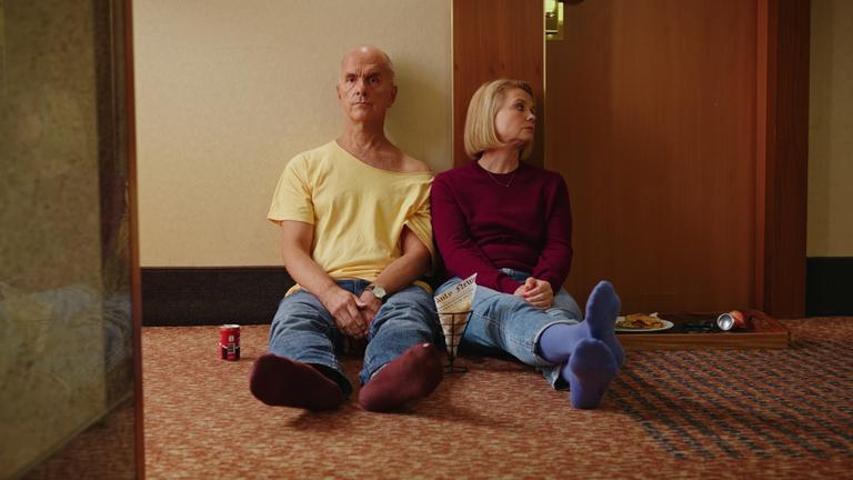 "Merz gegen Merz: Geständnisse": Erik (Christoph Maria Herbst) sitzt neben Anne (Annette Frier) auf dem Boden eines Hotelflurs. Zwischen ihnen stehen Getränkedosen und Fast Food. Während er mit ernstem Blick nach vorne schaut, sieht sie zur Seite.