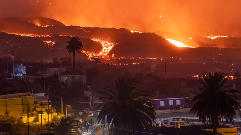 "La Palma - Protokoll eines Vulkanausbruchs": Ein Lavastrom fließt nachts unter einem rötlichen Himmel auf eine Ortschaft zu.