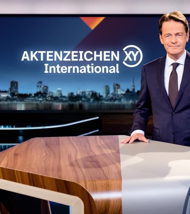 "Aktenzeichen XY... International": Rudi Cerne steht im Studio und lächelt in die Kamera.