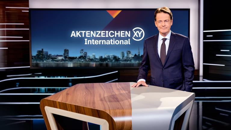"Aktenzeichen XY... International": Rudi Cerne steht im Studio und lächelt in die Kamera.