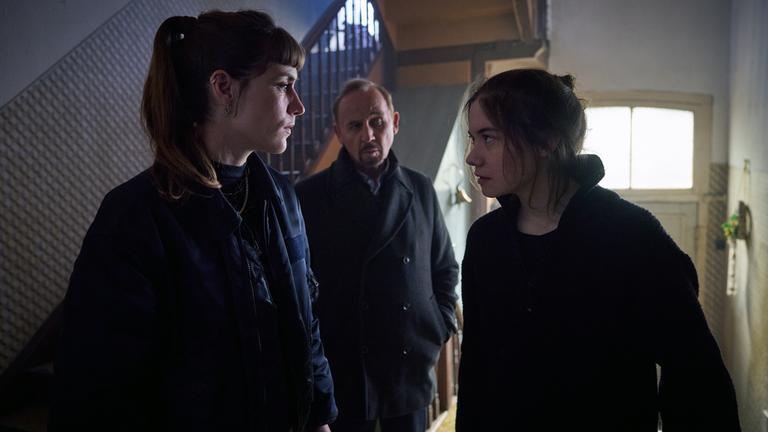 „STRALSUND – Dunkle Tiefen“: Jule Zabek (Sophie Pfennigstorf), Karl Hidde (Alexander Held) und Ella Brodersen (Hannah Schiller) stehen in einem Hausflur. Hinter den Personen ist eine alte Haustür mit Oberlicht.