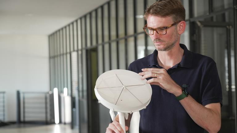 "WISO-Dokumentation: Zeitenwende: Hightech aus Deutschland": Lutz Stenvers blickt auf Modell-Teleskop in seiner Hand.