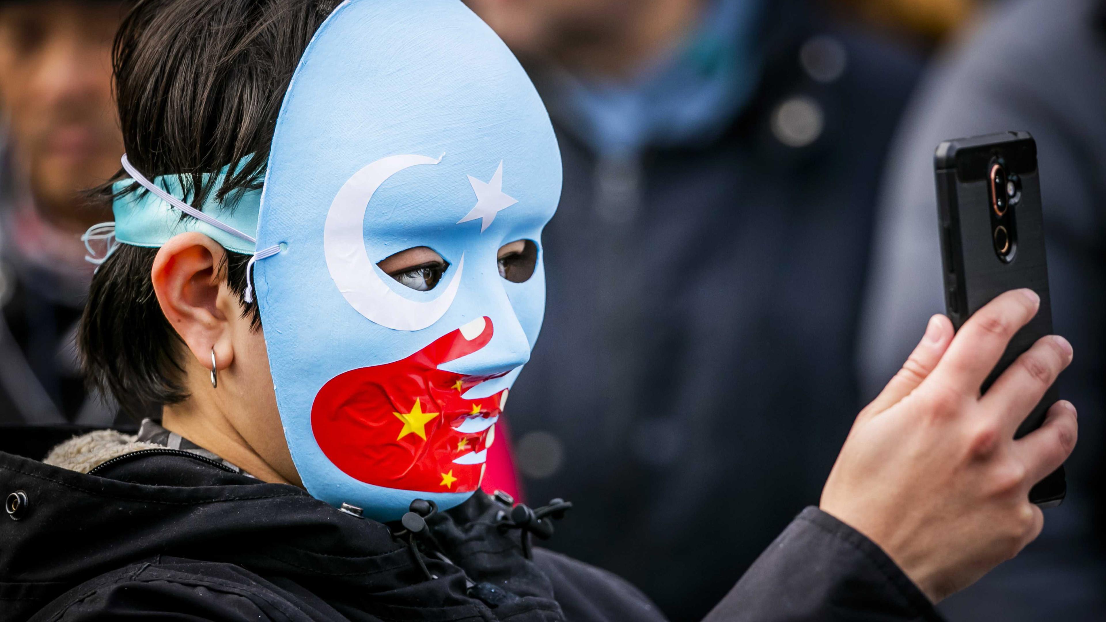 Person mit Maske; auf Maske Zeichen für Uiguren Wiederstand