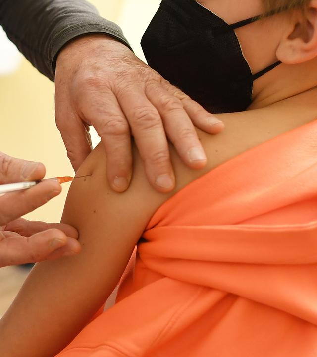 KInd im orangefarbenen Pulli wird geimpft