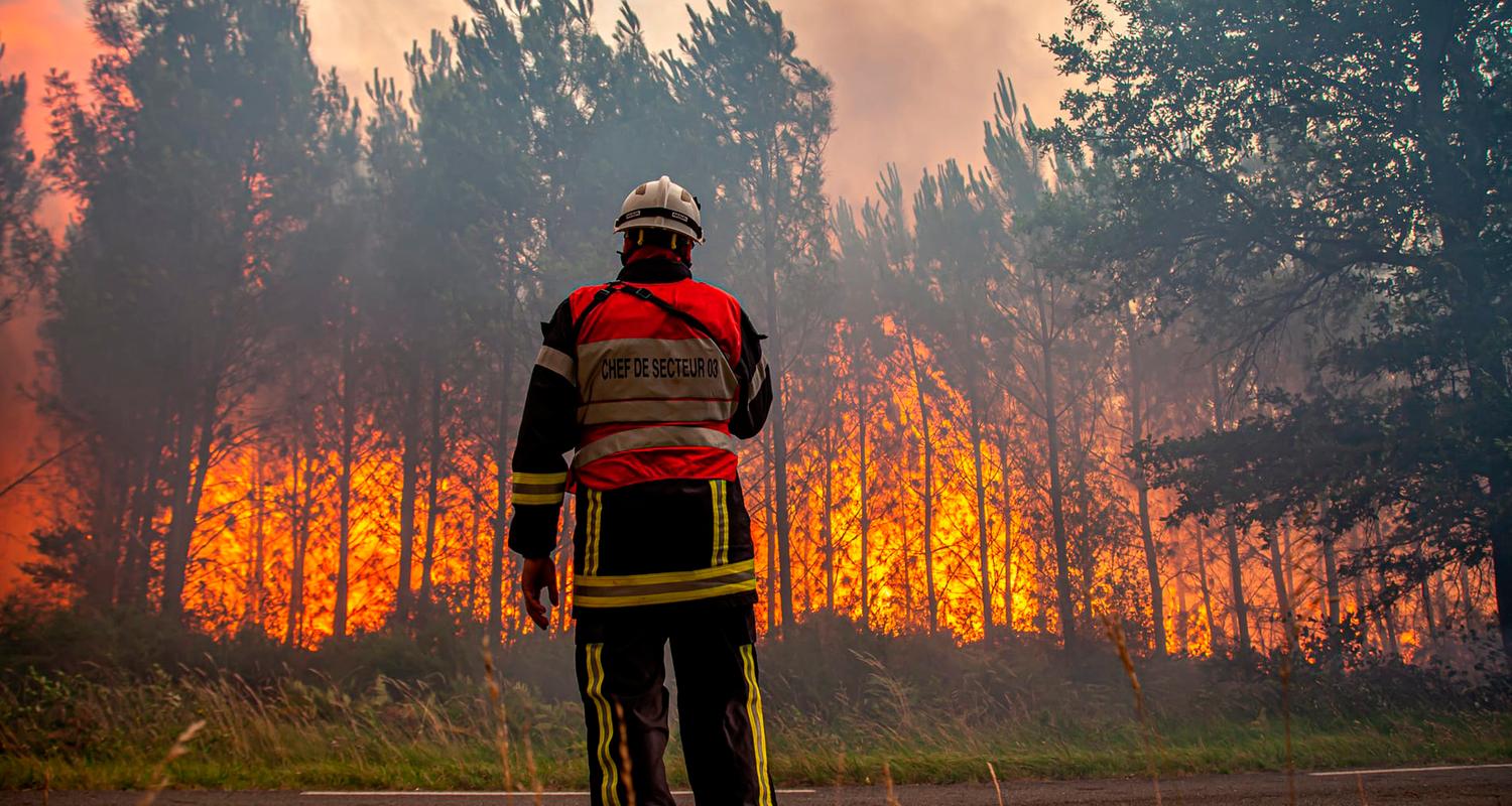 16.07.2022, Frankreich, Landiras: Ein Feuerwehrmann steht vor einem lichterloh brennenden Wald