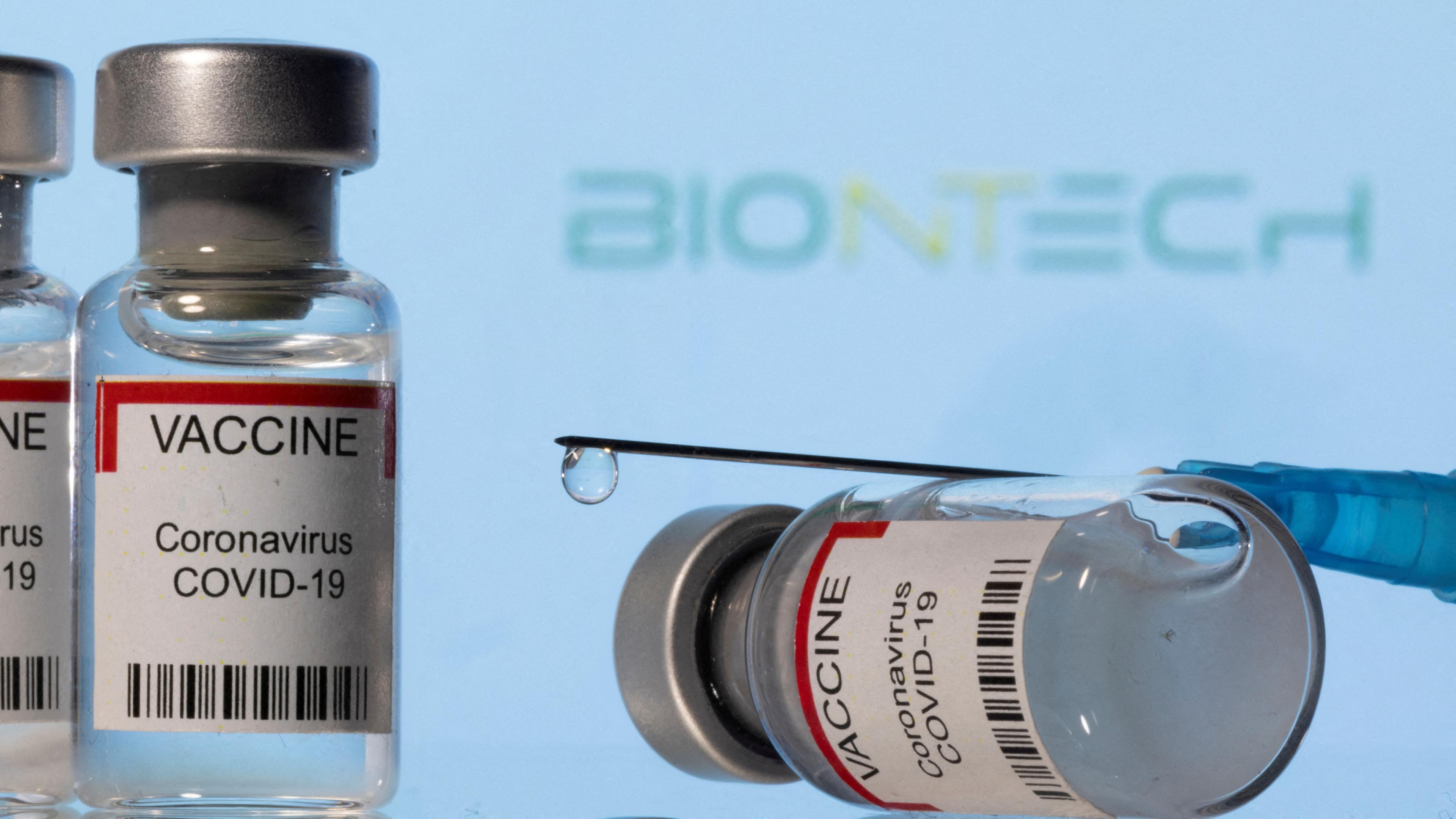 Fläschchen und eine Spritze mit dem Coronaimpfstoff liegen auf einer Fläche, das Biontech-Logo ist im Hintergrund zu sehen, Zenica, 08.08.2022