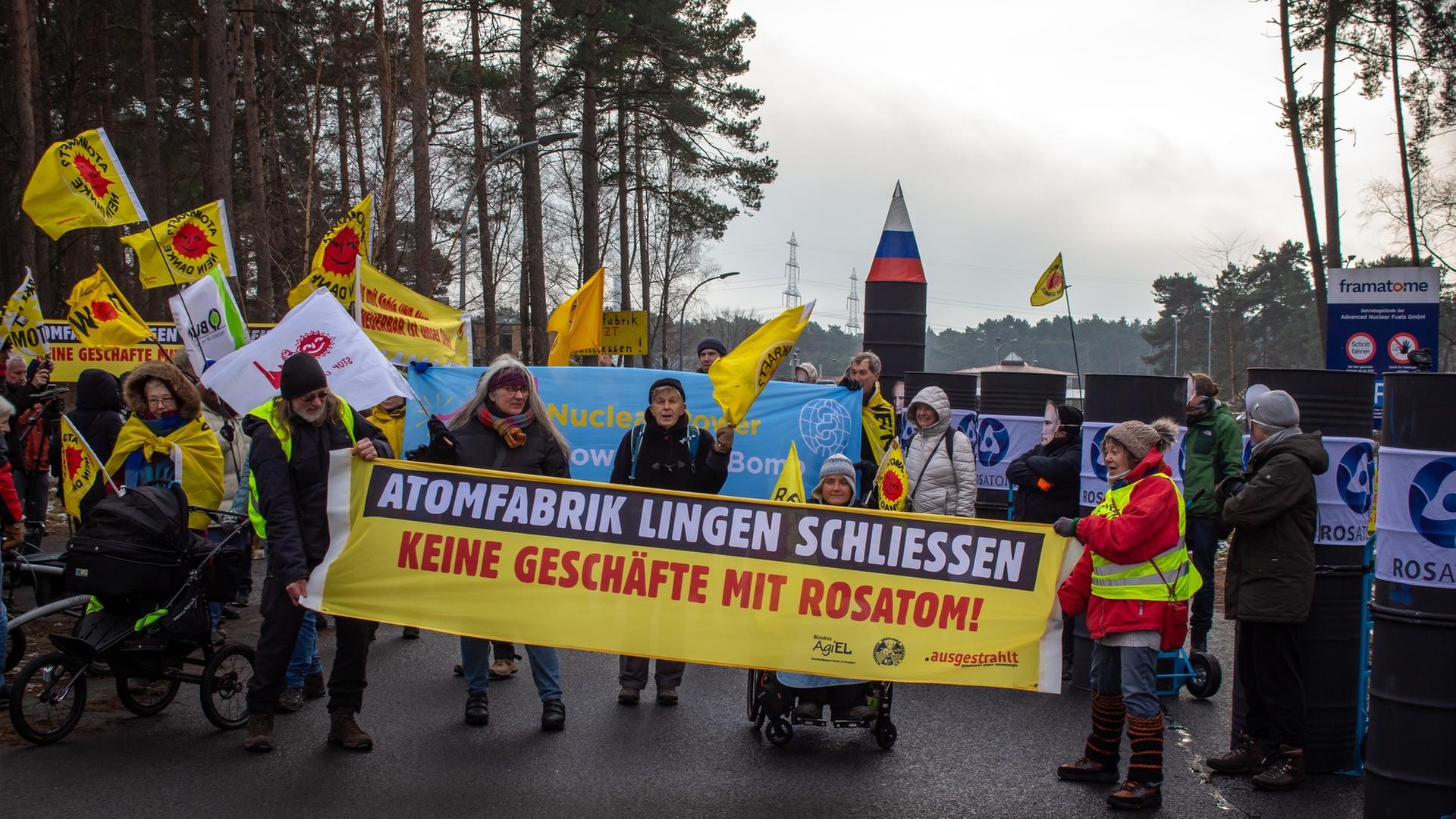 "frontal-Dokumentation: Russlands Atomgeschäfte - Europa in der Falle": Auf einer Straße im Wald stehen Demonstranten mit Transparenten und Bannern. Auf dem Transparent im Vordergrund steht "Atomfabrik Lingen schliessen - Keine Geschäfte mit Rosatom!"