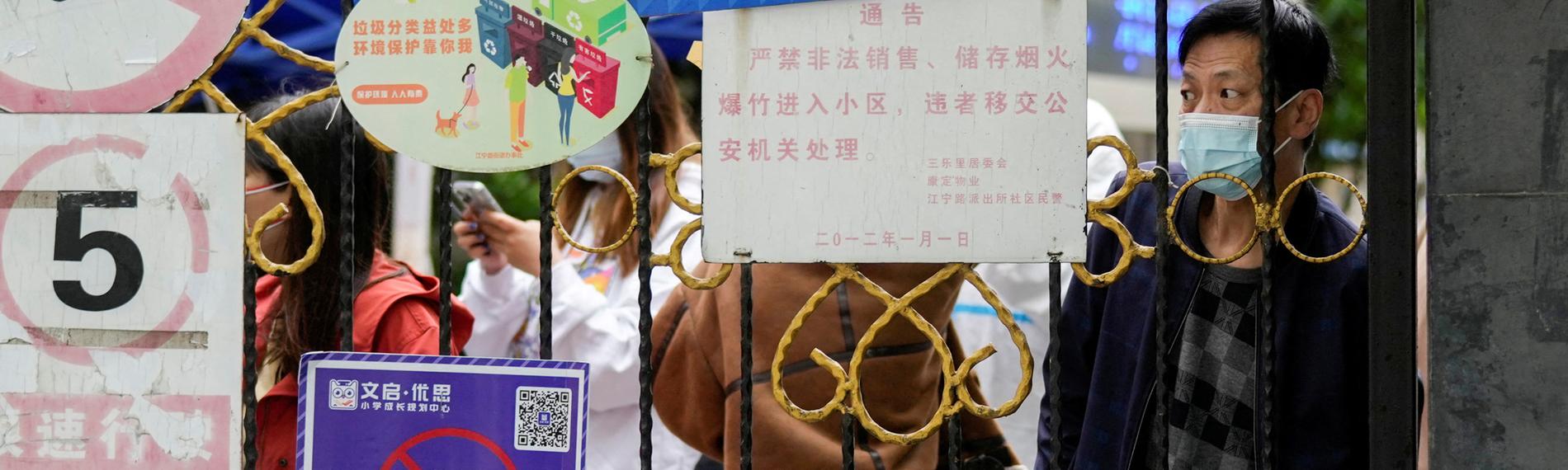 Chinesen vor einer Absperrung zu einem Wohngebiet