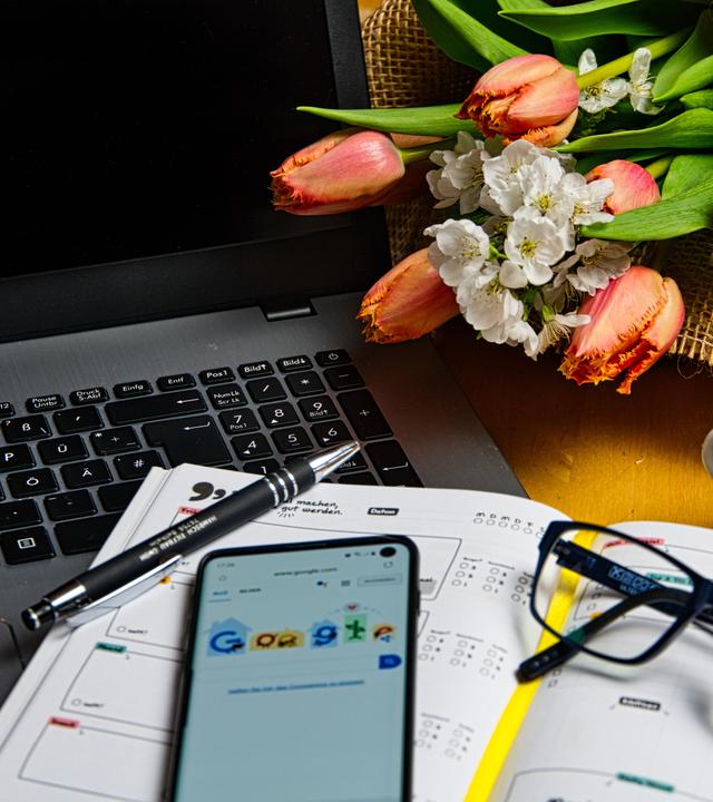 Homeoffice Arbeitsplatz mit Kalender im Vordergrund und Blumenstrauß