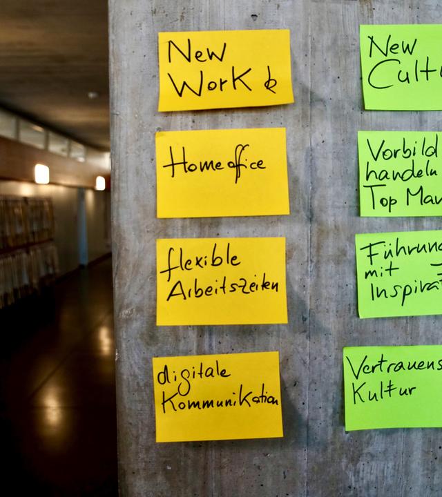  An einer Betonwand kleben Post-Its mit Stichwörtern in verschiedenen Farben.