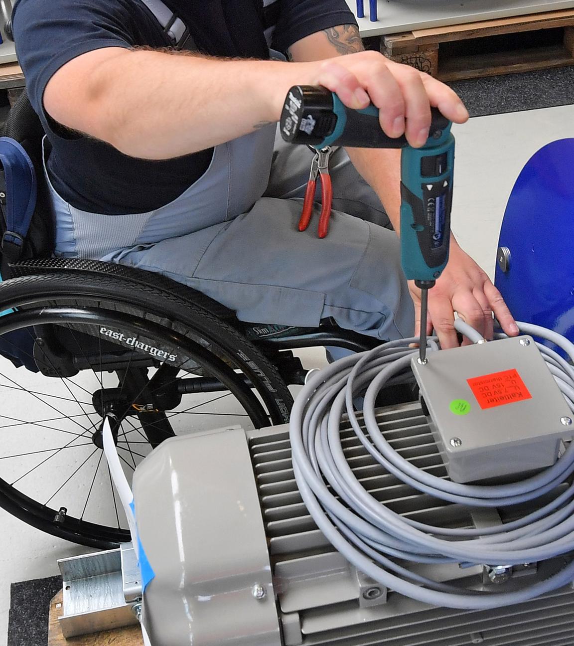 Behinderter in einem Rollstuhl verrichtet Montagearbeiten.