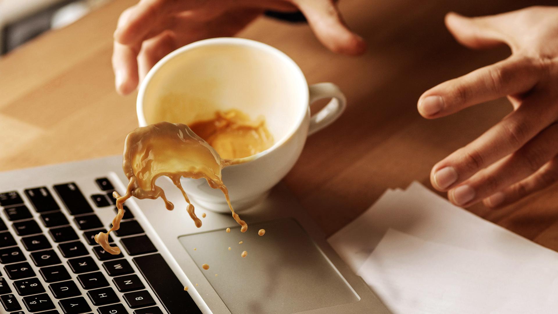 Kaffee aus einer Kaffeetasse wird über einem Laptop verschüttet