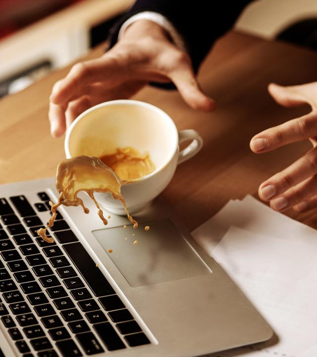 Kaffee aus einer Kaffeetasse wird über einem Laptop verschüttet