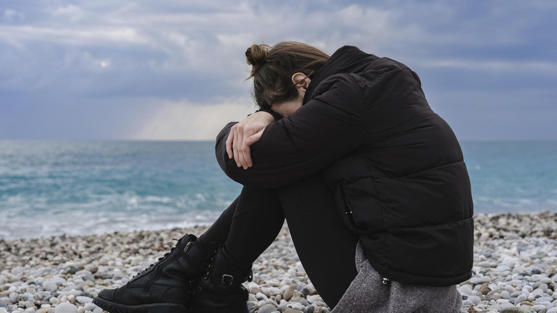 Junge Frau sitzt am Boden, den Kopf nach unten gesenkt