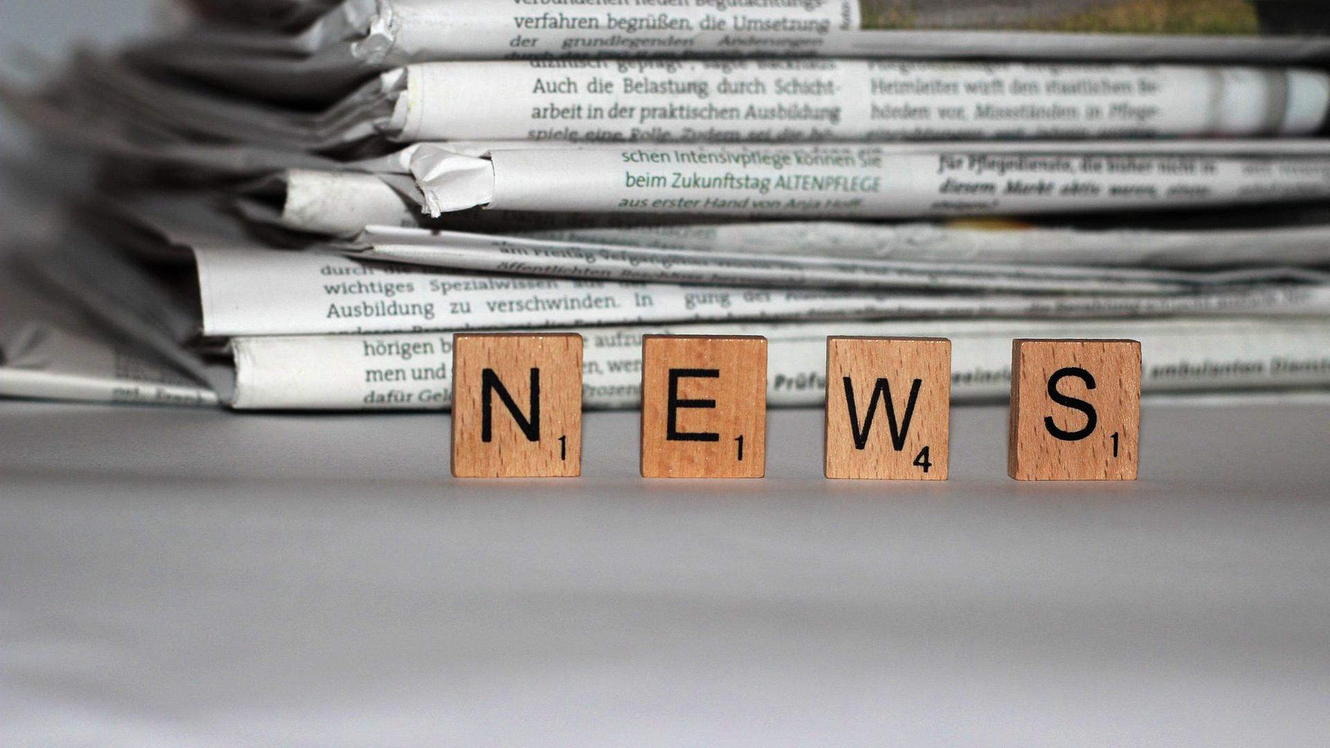 Zeitungstapel, im Vordergrund Spielsteine mit der AUfschrift "News"
