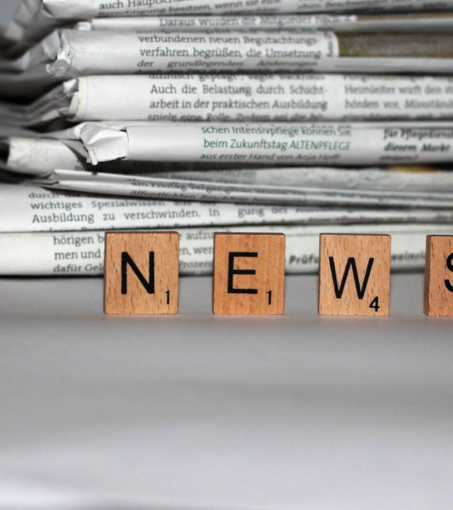 Zeitungstapel, im Vordergrund Spielsteine mit der AUfschrift "News"