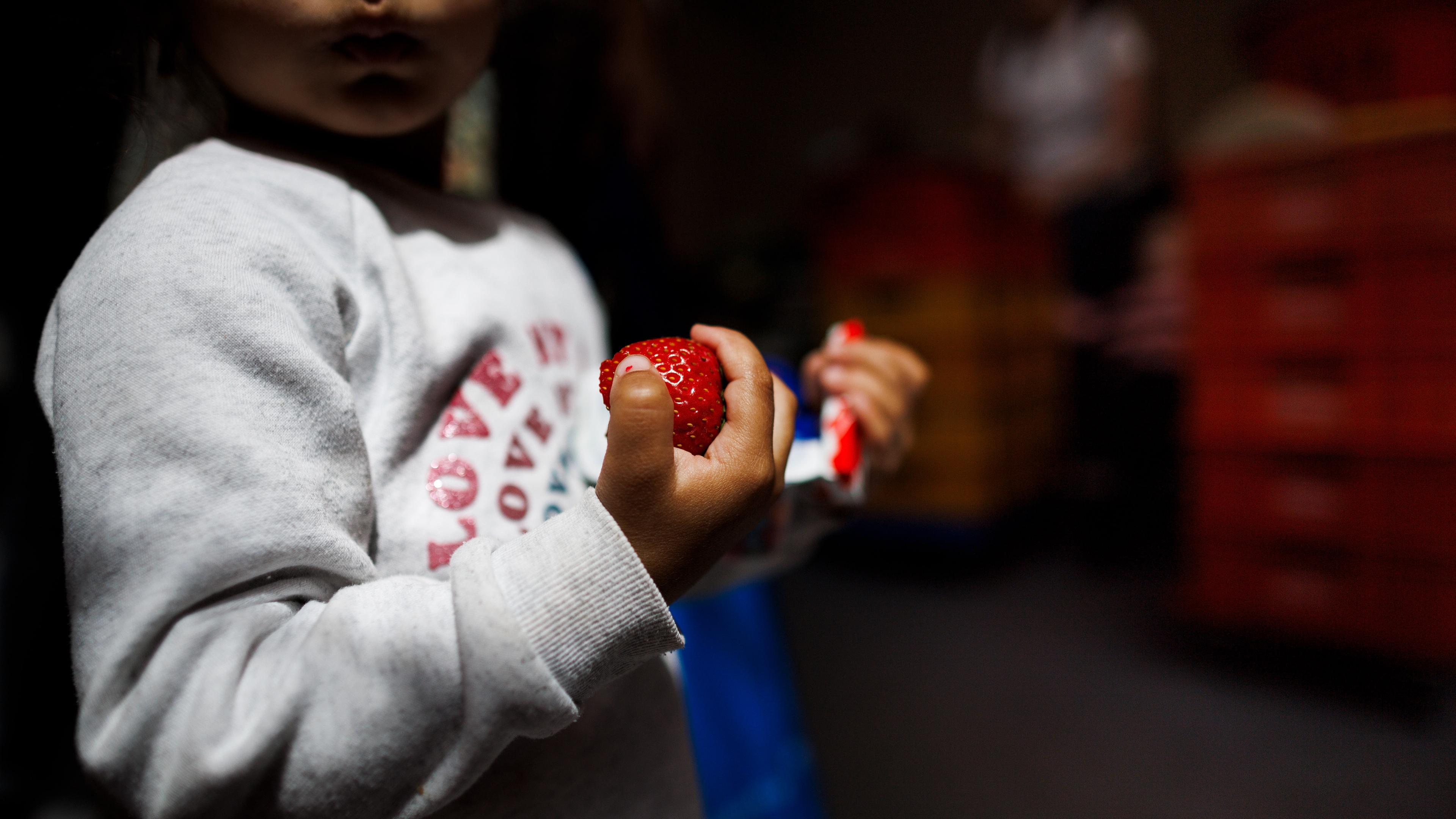 Kind hält Erdbeere und Kinderriegel in der Hand, Berlin, 04.07.2023.