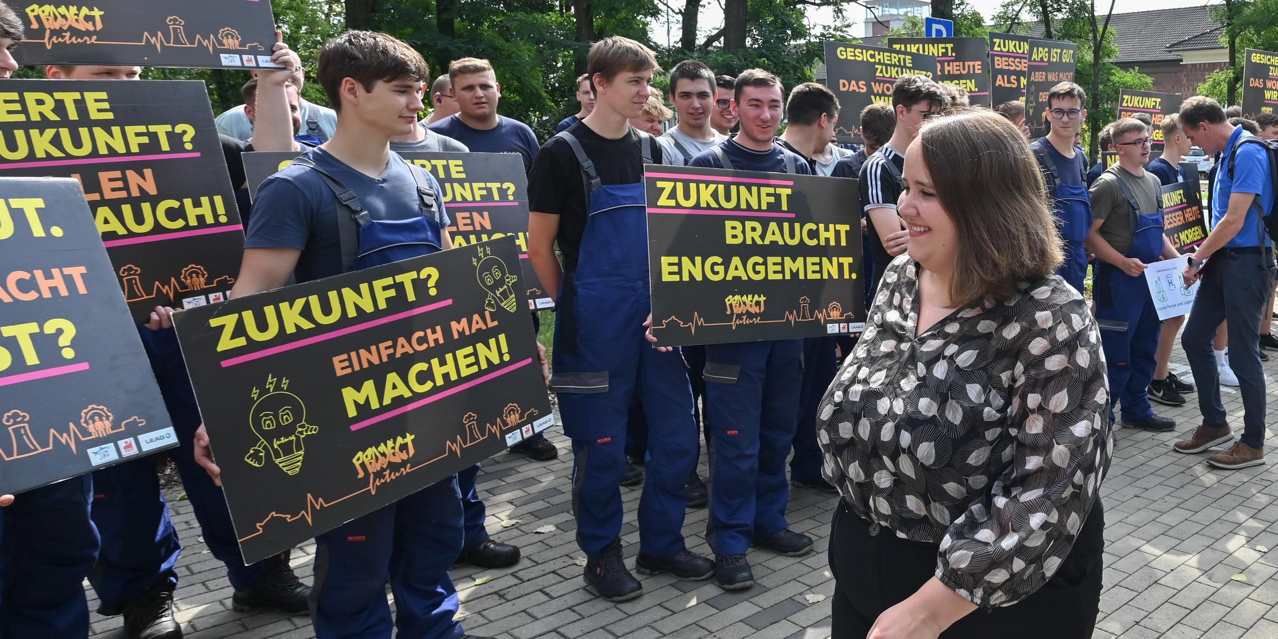 21.08.23, Cottbus: Ricarda Lang wird von einer Gruppe protestierender Lehrlinge begrüßt, die Plakate hochhalten.