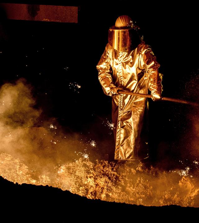 Mann steht an der Abstichrinne am Hochofen im Stahlwerk