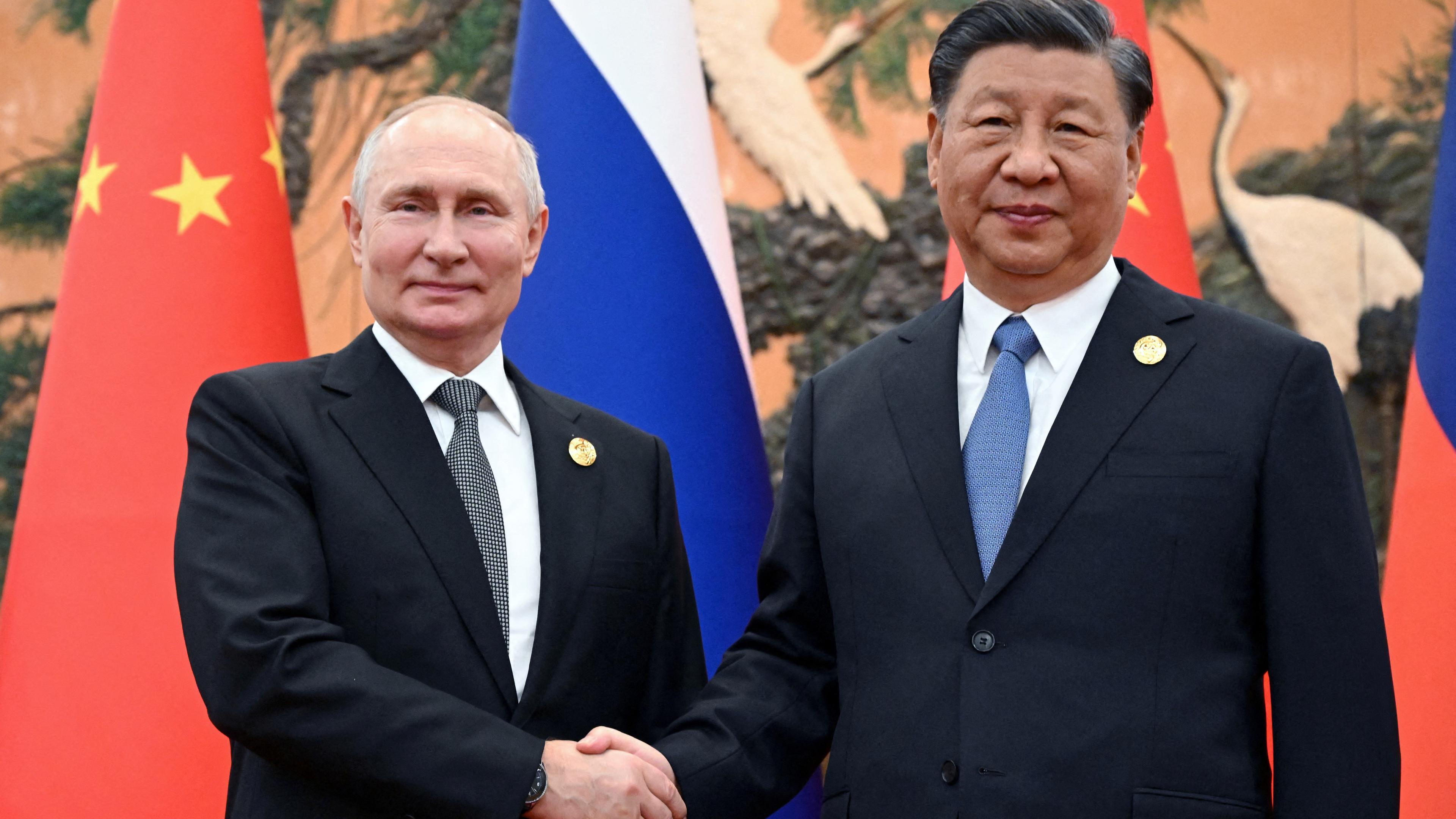 18.10.23, Beijing: Putin und Xi geben sich einen Handschlag vor den Fahnen ihrer Länder.
