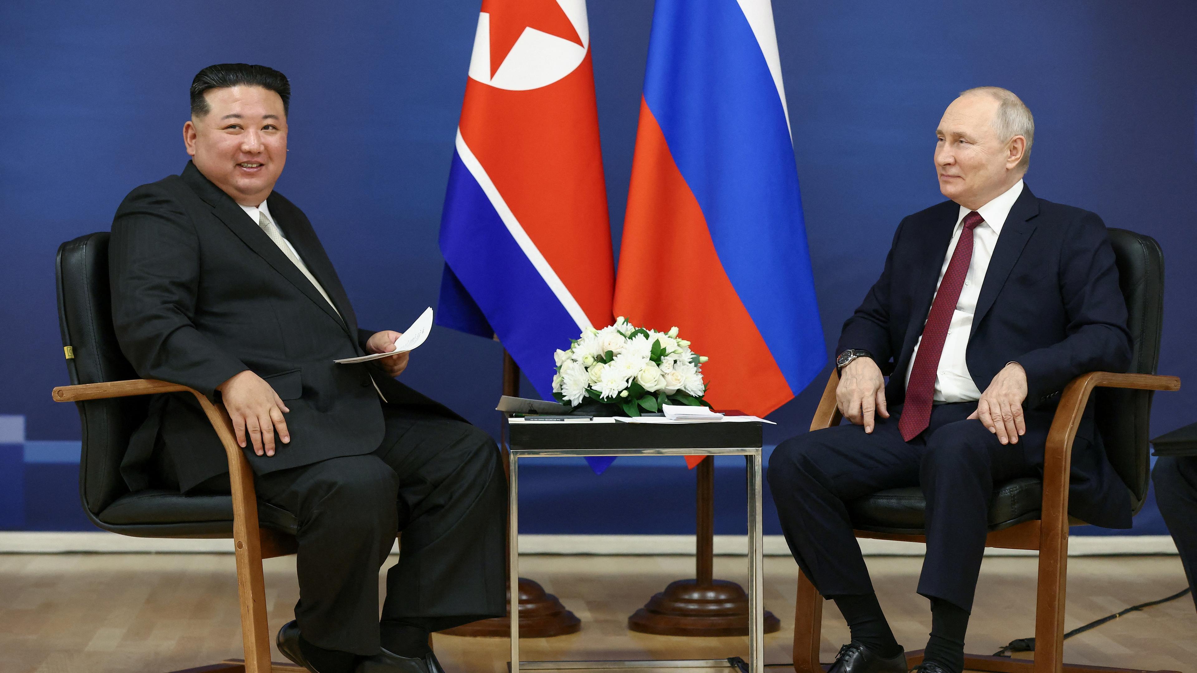 13.09.23, Russland: Der Nordkoreanische Präsident Kim und der russische Präsident Putin sitzen auf  Stühlen mit den jeweiligen Flaggen ihrer Länder im Hintergrund.