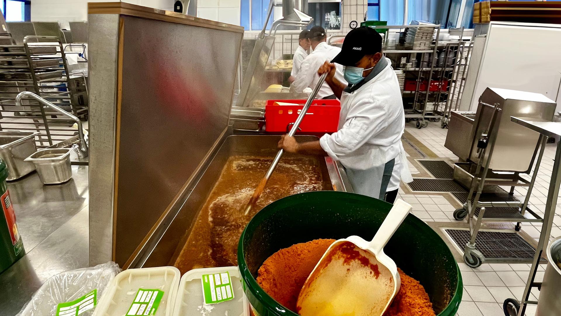 Koch rührt Saucenpulver in Großküchen-Tank.