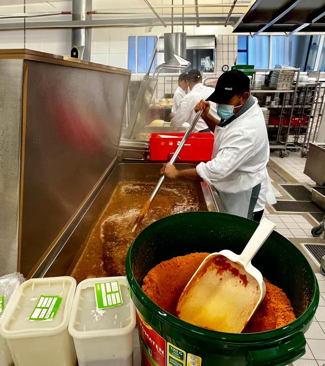 Koch rührt Saucenpulver in Großküchen-Tank.