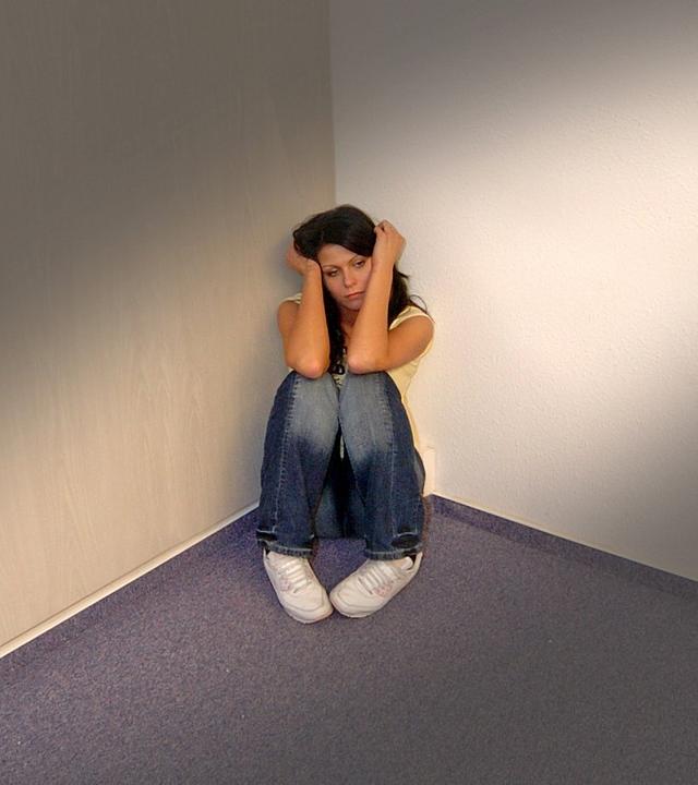 Frau sitzt verängstigt in der Ecke eines Raumes