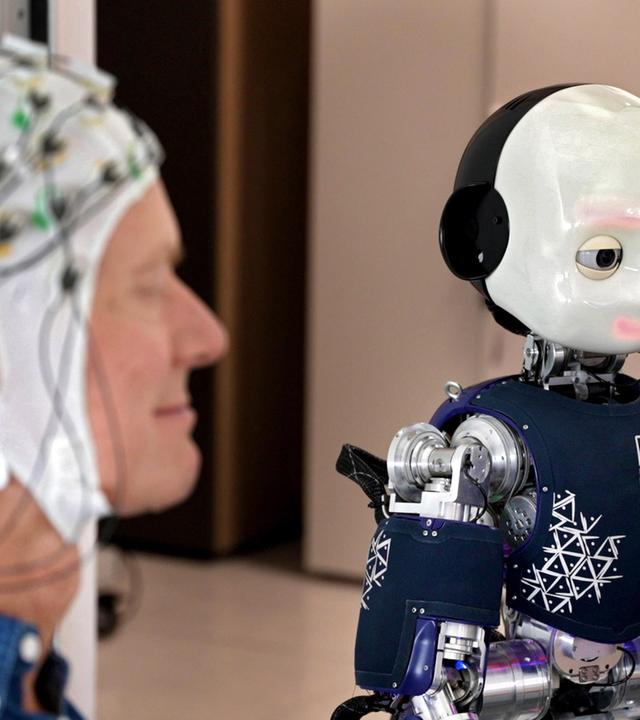 Ingolf Baur mit einer EEG-Haube neben einem humanoiden Roboter