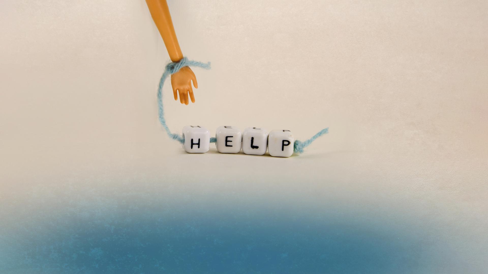 Kleine Hand hält ein Band mit Hölzkötzchen mit Aufschrift "Help"